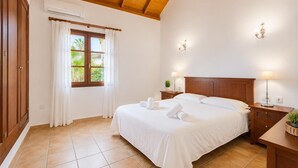 A bedroom with a wooden ceiling, a bed with white linens, two bedside lamps, and a window with curtains.