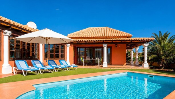 A swimming pool with blue tiles, surrounded by a patio area with lounge chairs and a covered seating area.
