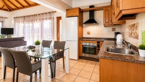 A modern kitchen with wooden cabinets, a built-in oven, and a glass dining table with wicker chairs.