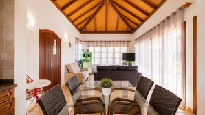 A living room with a glass table, wicker chairs, a sofa, a television, and a green cabinet.