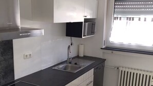 A modern kitchen with a black countertop, white cabinets, a built-in microwave, and a window with blinds. - NR 5 OG 3 ZKB for families and companies (Fuldatal)