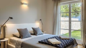 A bedroom with a large bed, two bedside lamps, a window with curtains, and a view of greenery outside. - Villa Veronika – Stone design villa of tranquility (Vabriga)