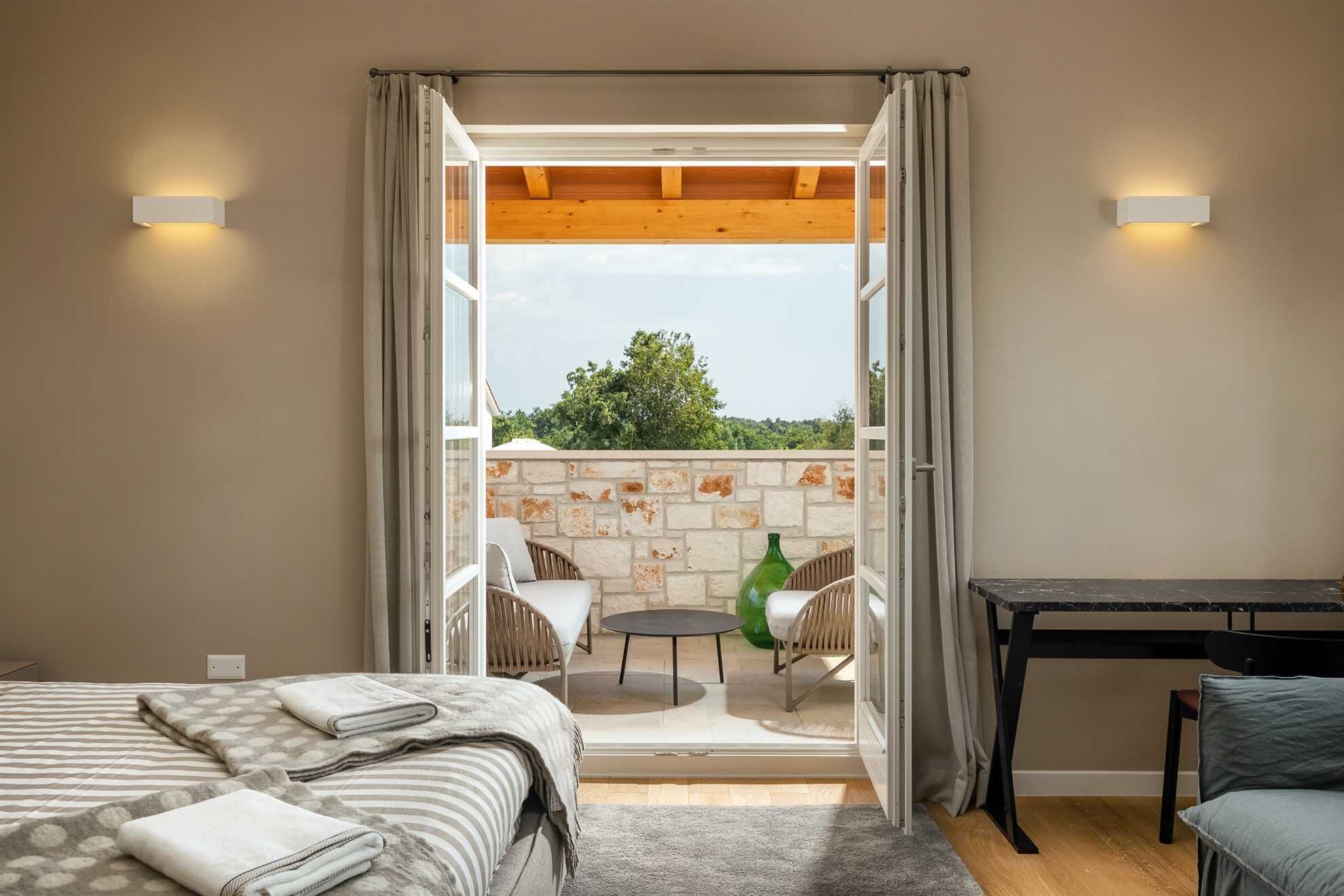 A bedroom with a bed, a small table, and a view of an outdoor balcony with a table and chairs.