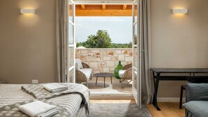 A bedroom with a bed, a small table, and a view of an outdoor balcony with a table and chairs. - Villa Veronika – Stone design villa of tranquility (Vabriga)
