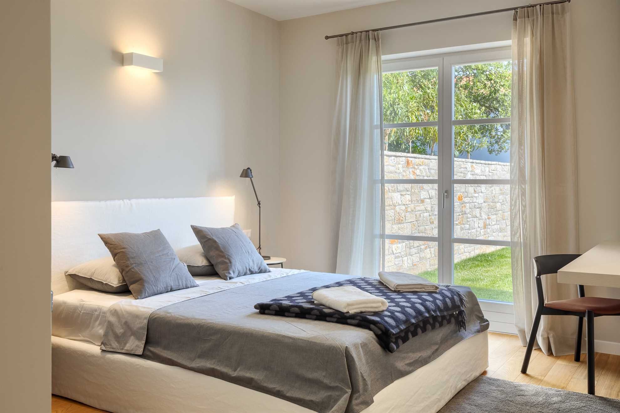 A bedroom with a large bed, a desk, and a window with curtains.