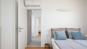 A bedroom with a bed, pillows, a bedside table, a wall-mounted air conditioner, and a door leading to another room. - B&M Adria Vista – Designer apartment in Novigrad (Novigrad)