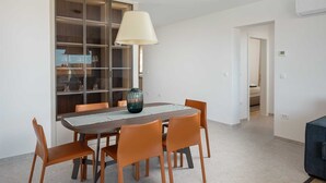 A dining area with a round table, six chairs, a hanging light fixture, and a glass cabinet with shelves. - B&M Adria Vista – Designer apartment in Novigrad (Novigrad)