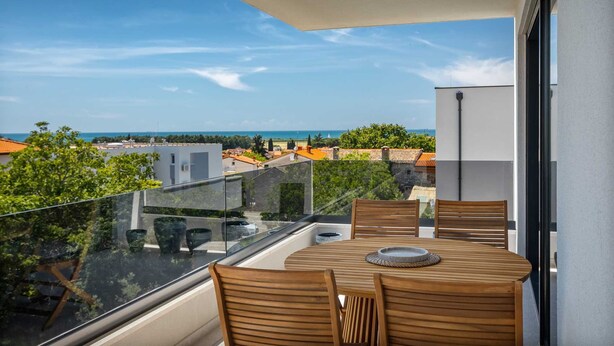 A balcony with a wooden table and chairs, offering a view of the sea and surrounding buildings. - B&M Adria Vista – Designer apartment in Novigrad (Novigrad)