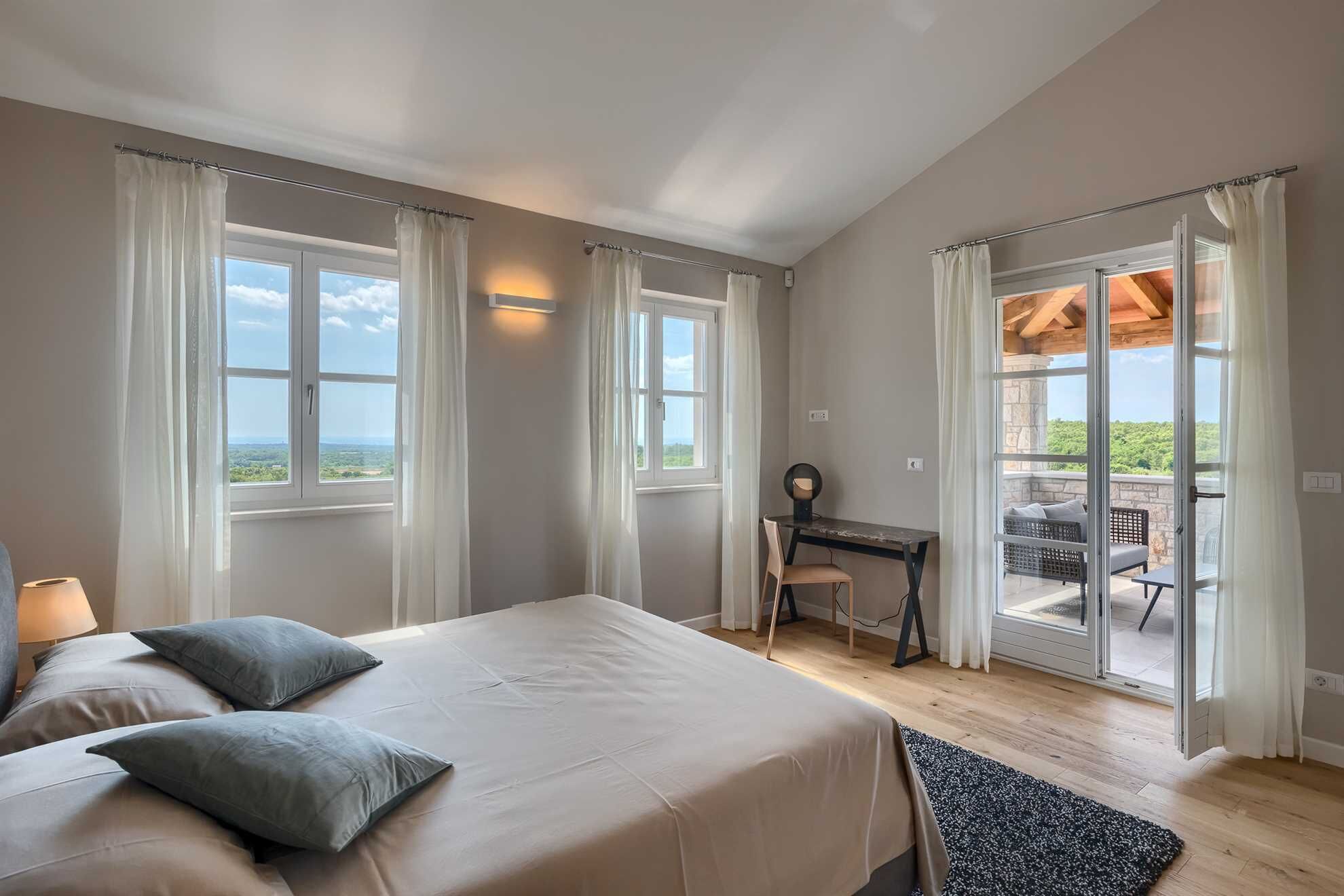 A bedroom with a bed, a desk, and a view of the outdoors.