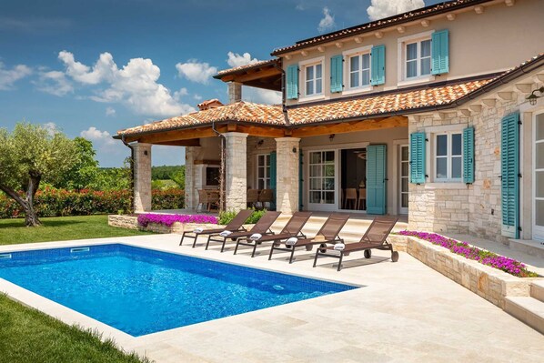 Una casa de dos pisos con piscina, mobiliario de exterior y jardín.