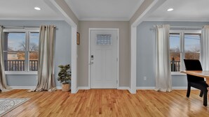 Um quarto amplo com piso de madeira, uma porta branca e janelas grandes com cortinas.