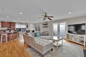 A spacious living area with a sofa, ottoman, and a TV on a stand.