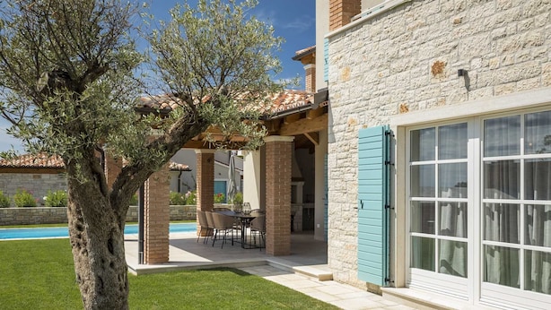A house with a stone facade, a covered patio with a table and chairs, and a swimming pool in the background. - Villa Oaza – A Stone Oasis with Sea View (Vabriga)