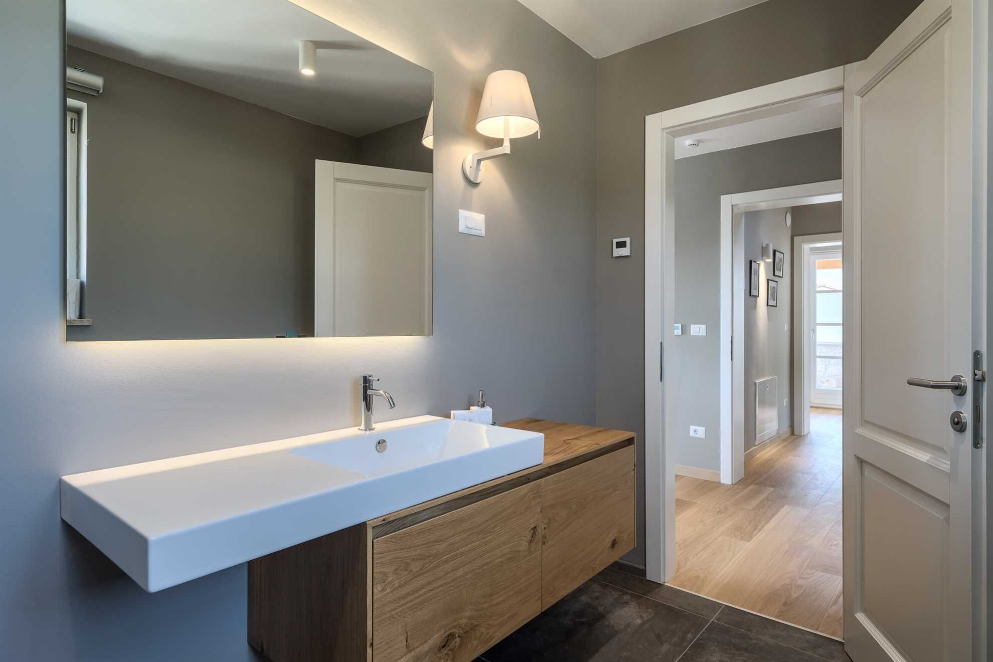 A modern bathroom with a long white sink, wooden vanity, and a wall-mounted mirror.