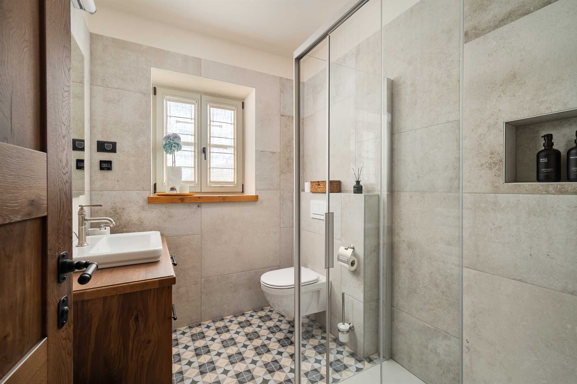 Ein modernes Badezimmer mit einem Holzwaschtisch, einer Toilette, einer Duschkabine aus Glas und einem Fenster mit einer Pflanze.