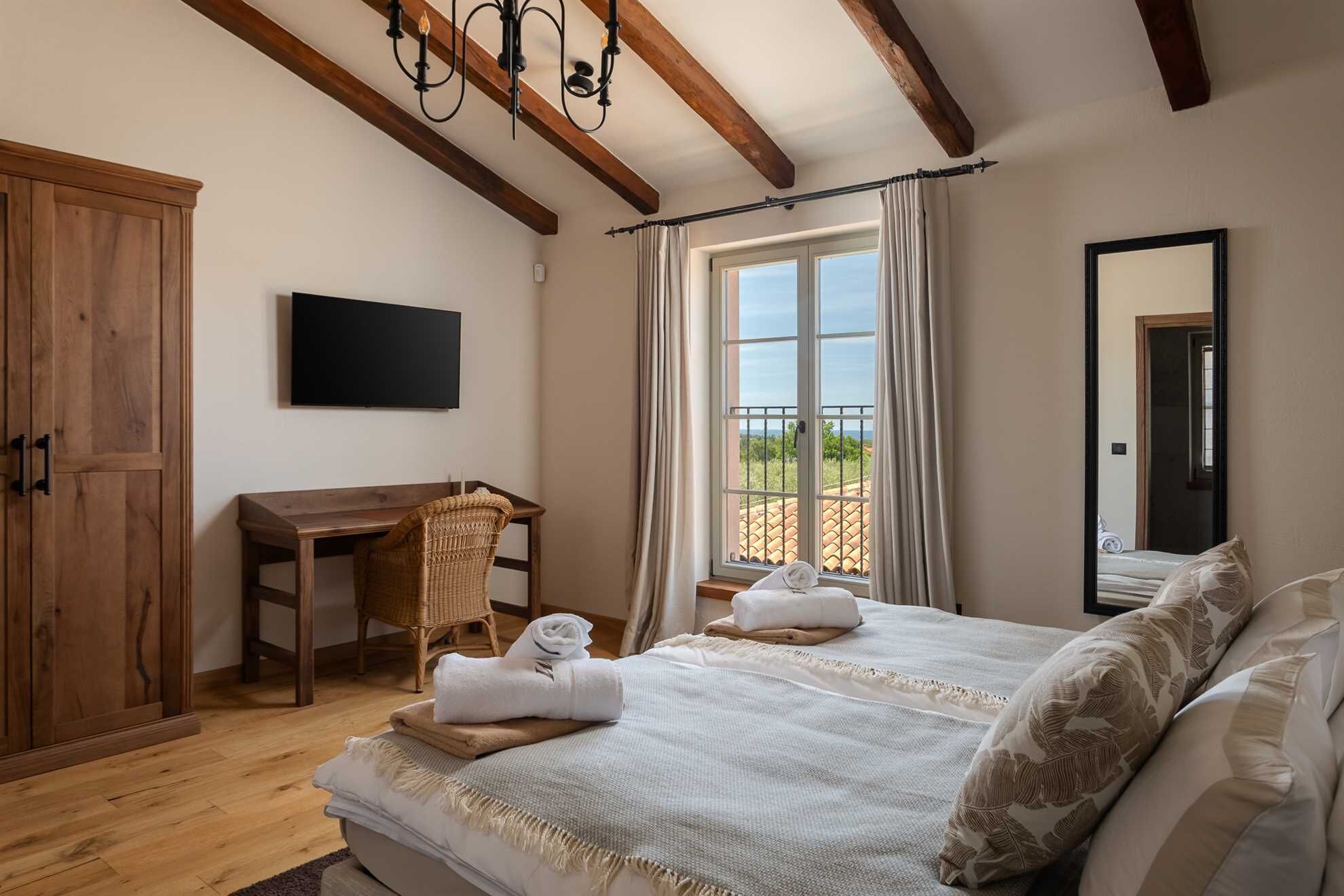 Une chambre à coucher comprenant un lit, un bureau, une chaise, une armoire et une fenêtre donnant sur un beau paysage.