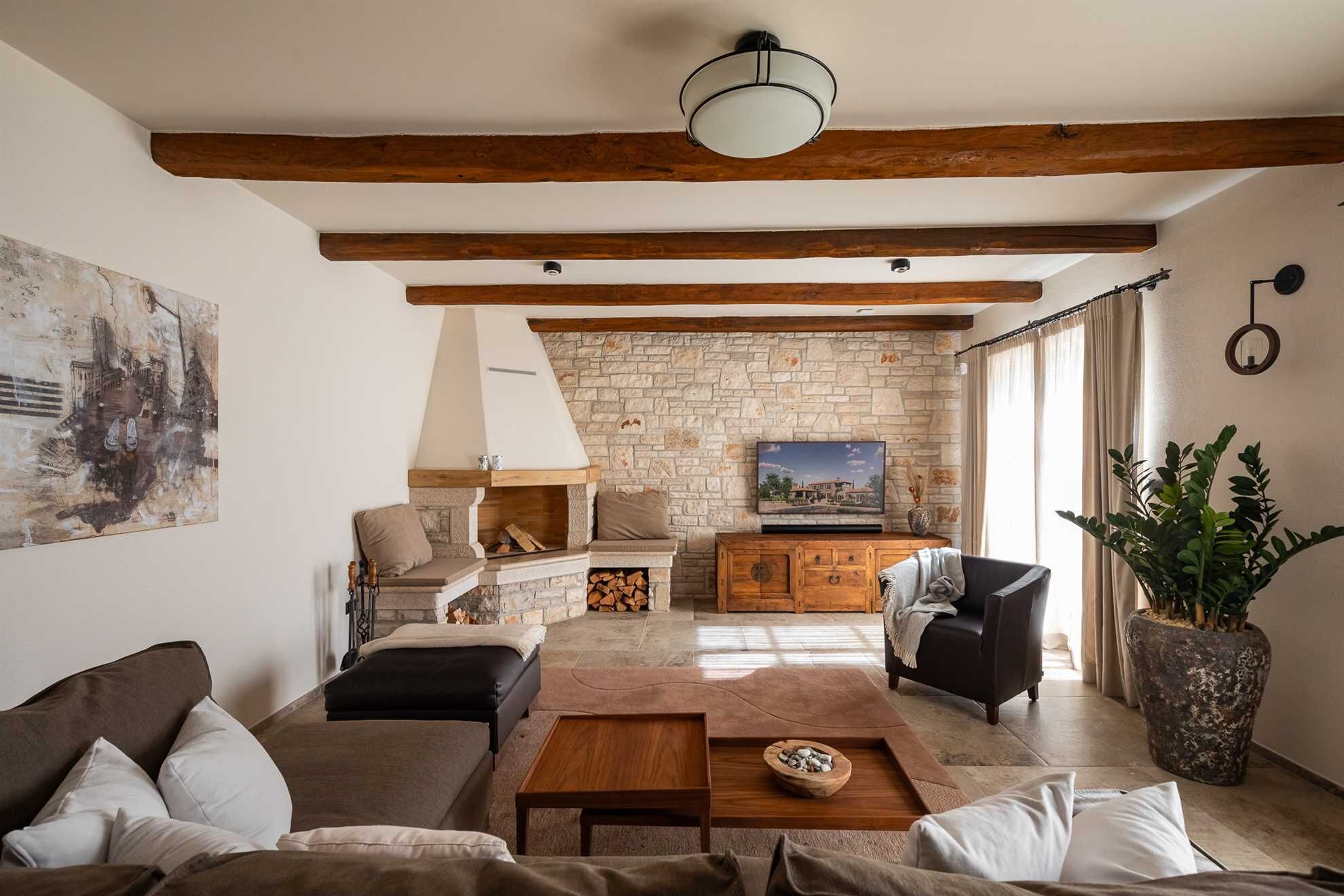 Una sala de estar acogedora con chimenea de piedra, vigas de madera, un sofá, una mesa de centro y una planta grande en maceta.