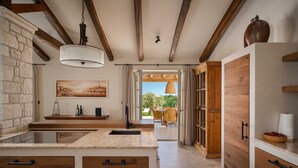 A modern kitchen with a stone wall, wooden beams, and a view to an outdoor dining area. - Villa Olive View – Your Exclusive Retreat (Vabriga)