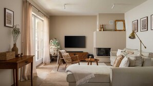 Un salon comprenant un canapé, un fauteuil, un téléviseur, une cheminée et une grande fenêtre avec des rideaux.
