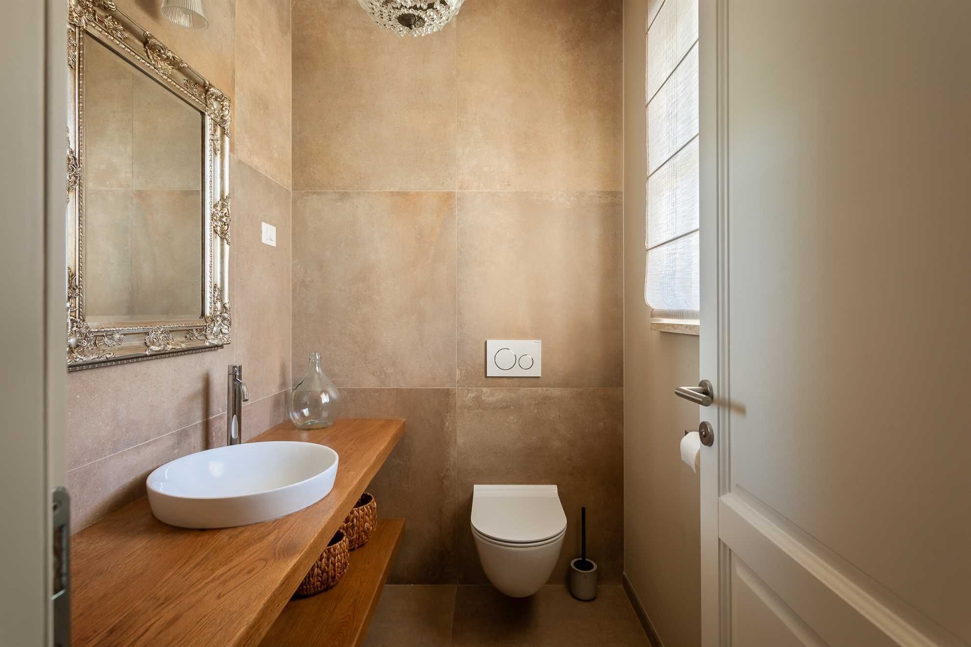 A bathroom with a wooden vanity, a white sink, a toilet, and a mirror with an ornate frame.