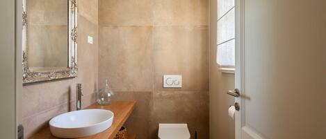 A bathroom with a wooden vanity, a white sink, a toilet, and a mirror with an ornate frame.