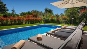 Une piscine entourée de verdure et de fleurs, avec des chaises longues et un parasol.