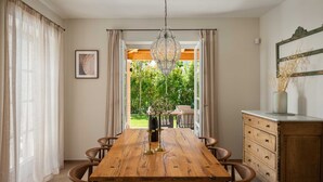 Un coin repas comprenant une table en bois, six chaises, un lustre et une vue sur l’extérieur.