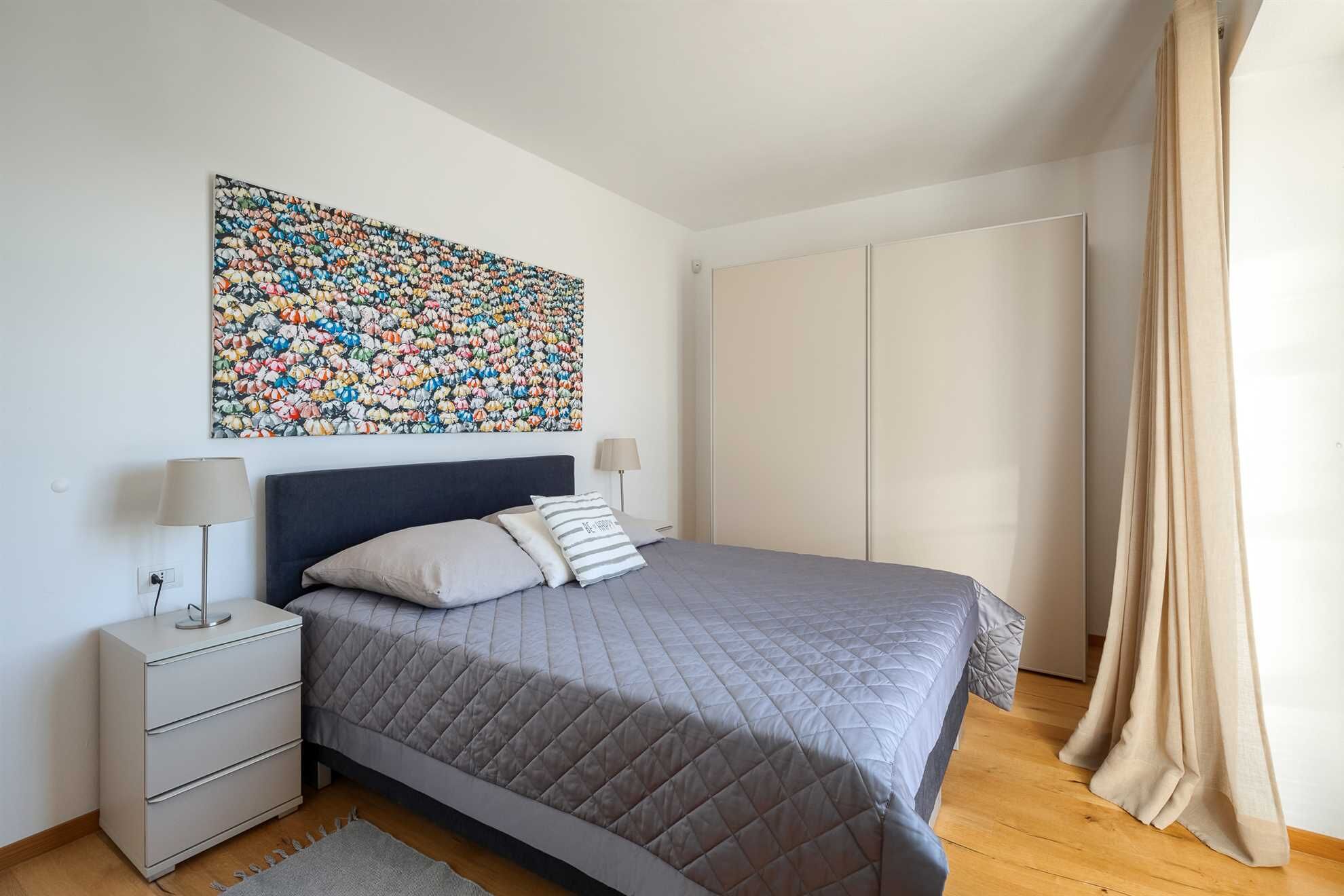 Une chambre à coucher comprenant un lit, des tables de chevet, une armoire et une œuvre d’art florale aux couleurs vives accrochée au mur.