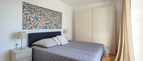 Une chambre à coucher comprenant un lit, des tables de chevet, une armoire et une œuvre d’art florale aux couleurs vives accrochée au mur.