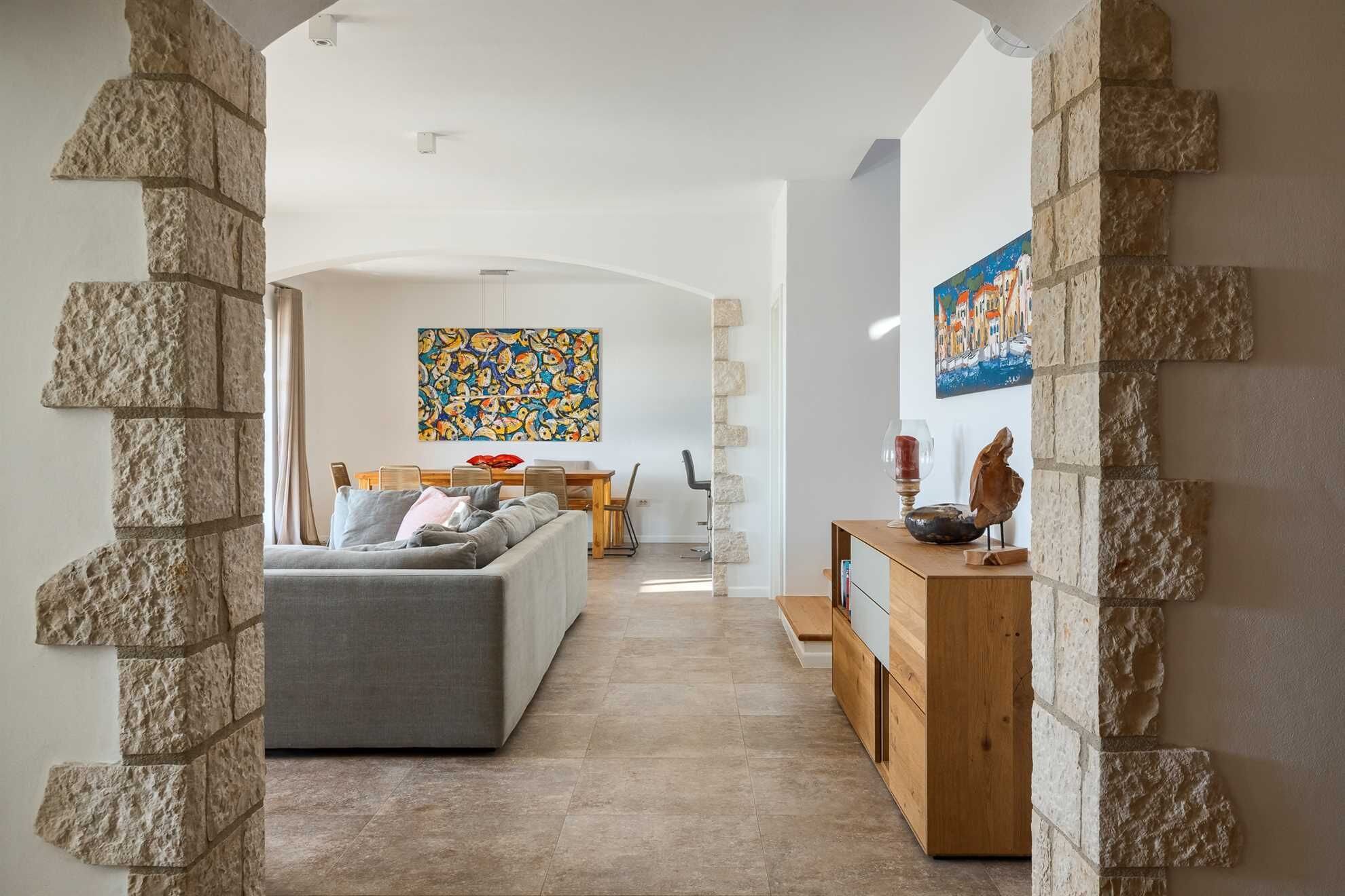 Een moderne woonkamer met een grijze bank, een houten eettafel met stoelen, en een accentmuur van steen.