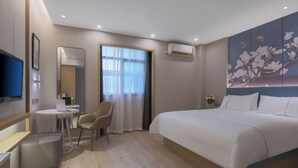 Habitación de hotel con cama, escritorio, silla, televisor y una ventana grande con cortinas.