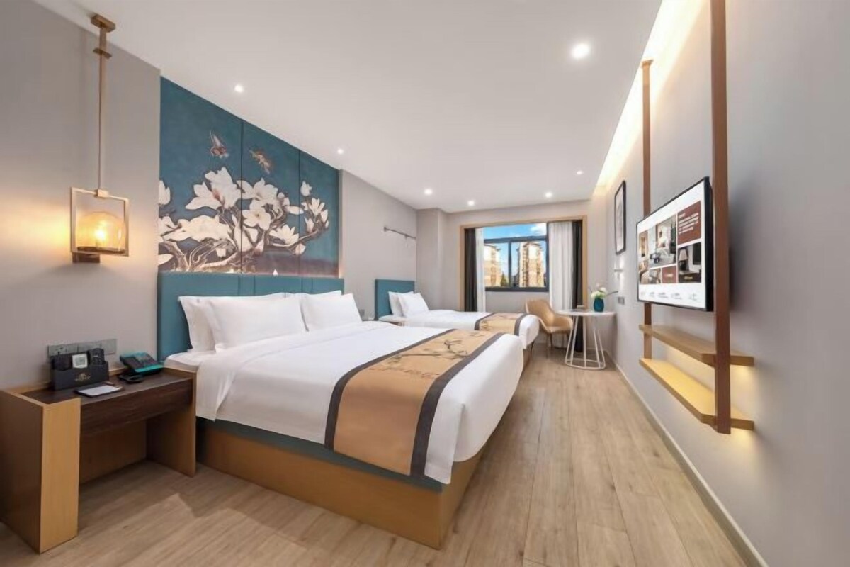 A modern hotel room with a large bed, bedside tables, a desk, and a view of the city.