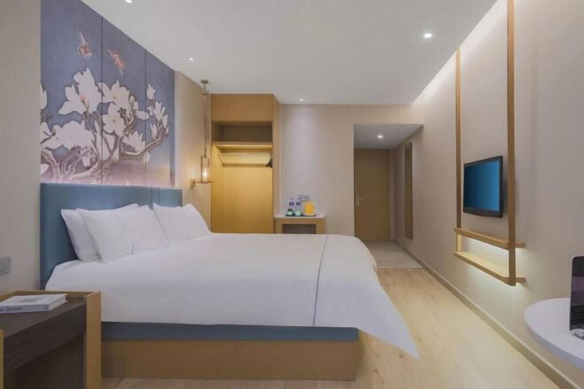 A modern hotel room with a large bed, a bedside table, a wall-mounted TV, and a decorative floral mural.