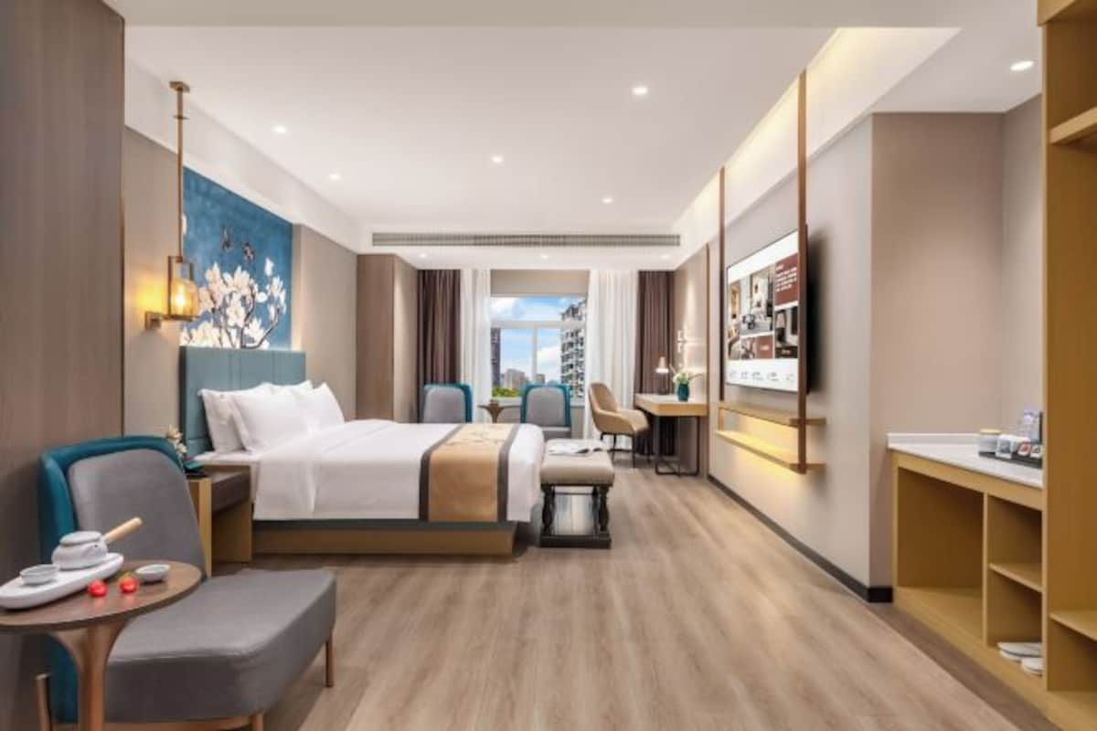 A hotel room with a bed, bedside table, chair, desk, and a view of the outdoors.
