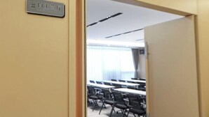 Ett konferensrum med bord och stolar, en namnskylt på väggen och ett tak med belysningsarmaturer.