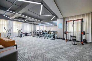 A gym with various exercise equipment, a patterned carpet, and a large window with curtains. - Magnolia Hotel (Nanjing Olympic Sports Center Branch) (Nanjing)