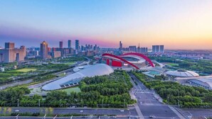 Vista aérea de una ciudad moderna con un puente rojo destacado, zonas verdes y una mezcla de rascacielos.