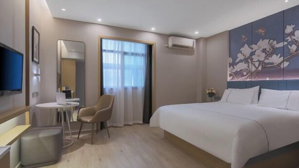 Habitación de hotel con cama, escritorio, silla, televisor y aire acondicionado.