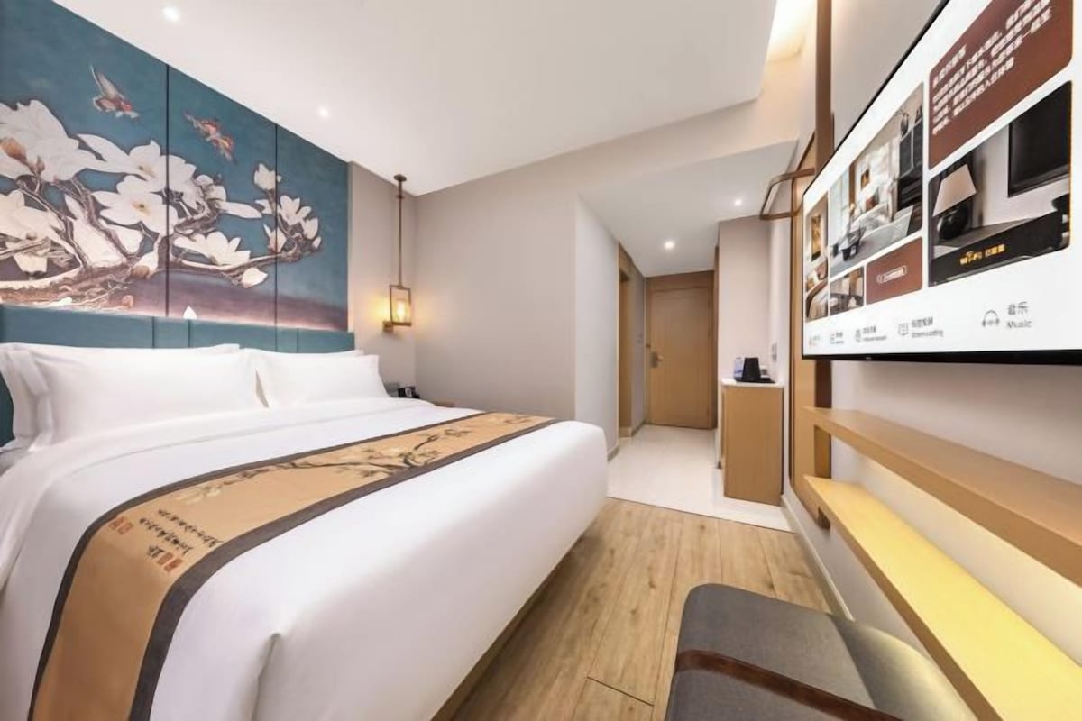 A hotel room with a large bed, a wall-mounted TV, and a wooden desk.