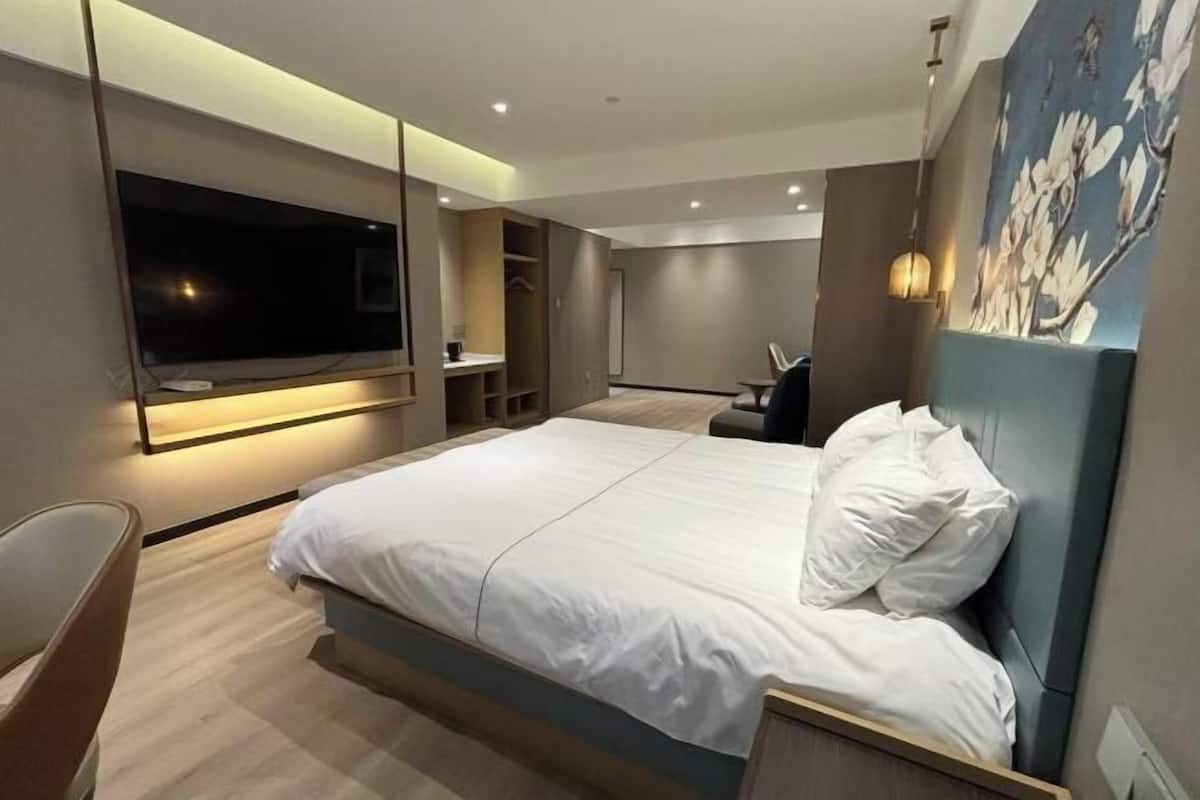 A modern hotel room with a large bed, a TV mounted on the wall, a desk, and a chair.