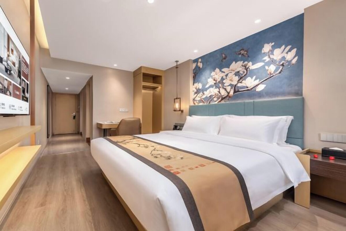 A hotel room with a large bed, a desk, and a wall-mounted artwork.