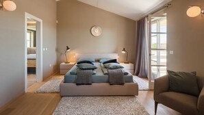 Une chambre à coucher avec un grand lit, deux lampes de chevet, une horloge ronde fixée au mur et une vue par la fenêtre.