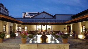 Un patio central con una fuente, plantas en macetas y un edificio con techo de tejas y columnas.