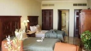 Una habitación de hotel con una cama, dos mesitas de noche, una silla y una pequeña mesa con un jarrón.