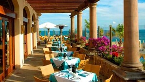 Un espacio de comedor al aire libre con mesas dispuestas para comensales, con vistas a un paisaje marino.