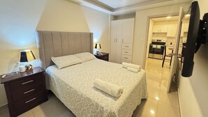 Ein Schlafzimmer mit Bett, Nachttischen, einem Kleiderschrank und Blick in die Küche.