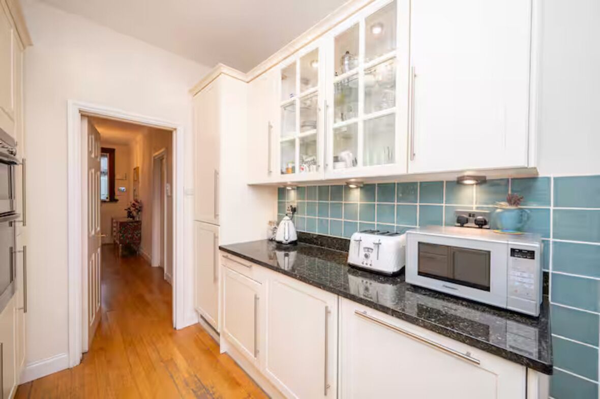 A kitchen with white cabinets, a microwave, a toaster, and a tiled backsplash.