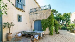 An outdoor dining area with a table and chairs, a potted plant, and a building with a balcony. - Nineteenth-century house with adjoining historic garden on the Stagnone of Marsala (Marsala)