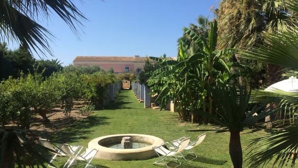 A garden with a circular water feature, lounge chairs, and a building in the background. - Nineteenth-century house with adjoining historic garden on the Stagnone of Marsala (Marsala)