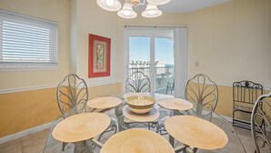 Un espace repas avec une table en verre entourée de chaises en métal, un grand vase décoratif au centre et un lustre.